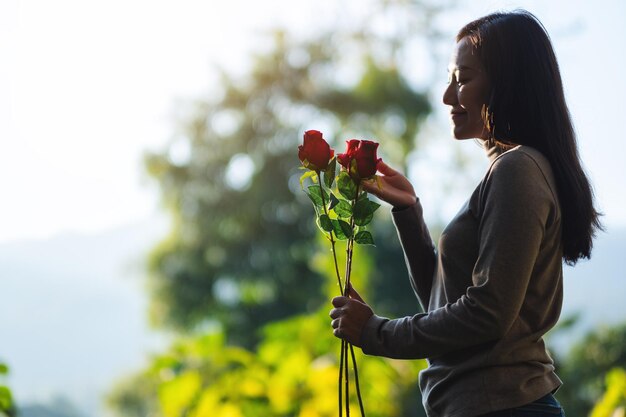 公園で赤いバラの花を保持している美しいアジアの女性のクローズアップ画像