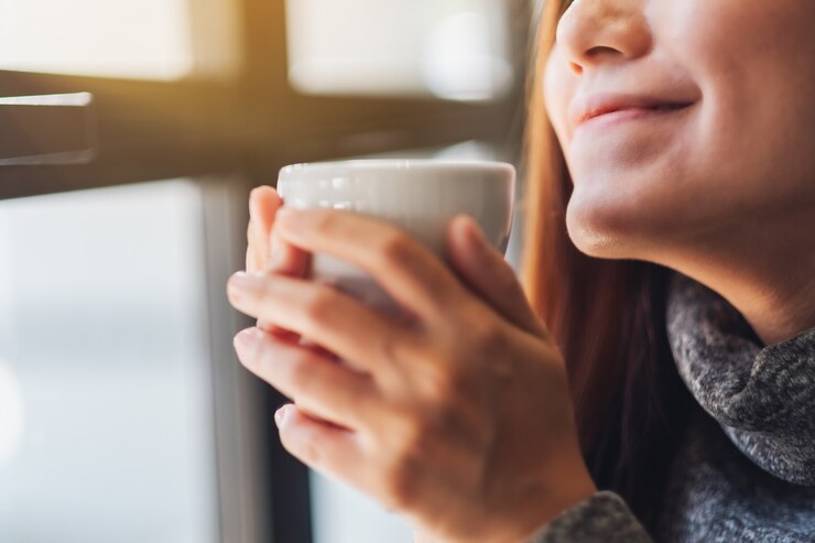 Photo ホットコーヒーのカップを保持し、匂いを嗅ぐ美しいアジアの女性のクローズアップ画像