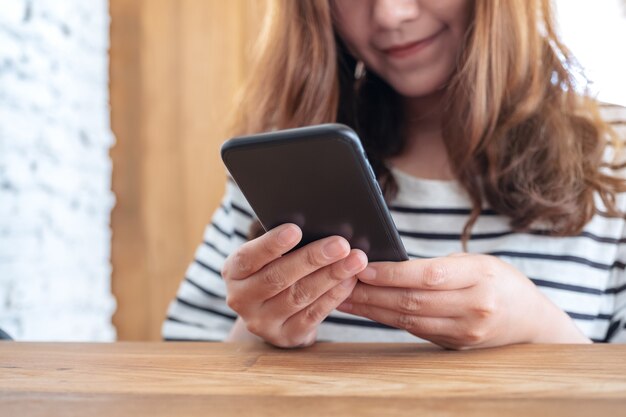 Immagine del primo piano di una bella donna asiatica che tiene, utilizzando e guardando smart phone nella caffetteria