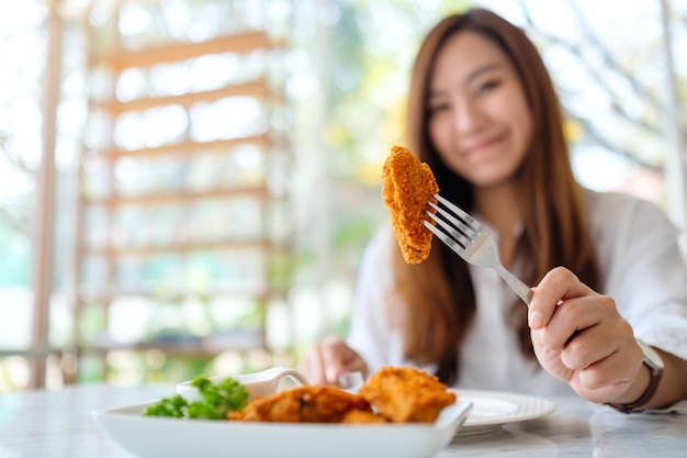 Closeup image of a beautiful asian woman showing and eating fried chicken in restaurant