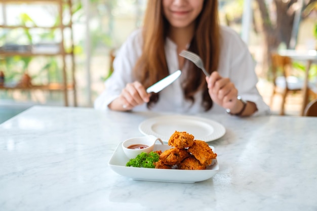 Immagine del primo piano di una bella donna asiatica che usa coltello e forchetta per mangiare pollo fritto al ristorante