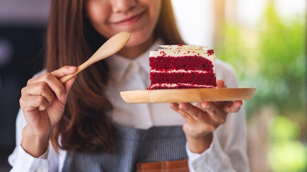 Immagine del primo piano di una bella donna chef femminile che cuoce e mangia un pezzo di torta di velluto rosso nel vassoio di legno