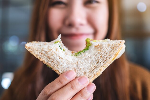 통밀 샌드위치 한 조각을 잡고 물고 있는 아름다운 여성의 클로즈업 이미지