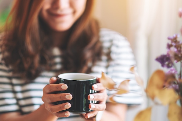 飲むためにホットコーヒーの黒いカップを保持している美しい女性のクローズアップ画像