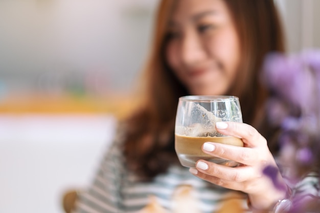 カフェで飲むためにアイスコーヒーのグラスを保持している美しい女性のクローズアップ画像