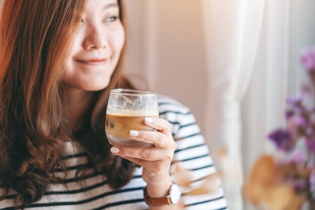 カフェで飲むためにアイスコーヒーのグラスを保持している美しい女性のクローズアップ画像