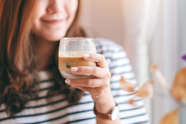 カフェで飲むためにアイスコーヒーのグラスを保持している美しい女性のクローズアップ画像