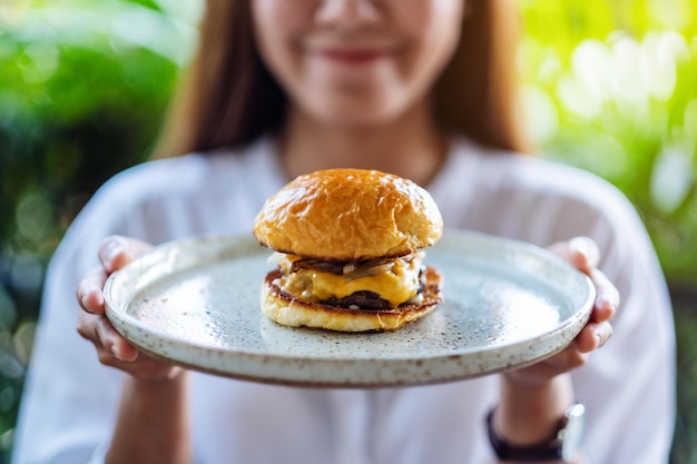 Closeup image of a beautiful woman holding a plate of beef hamburger