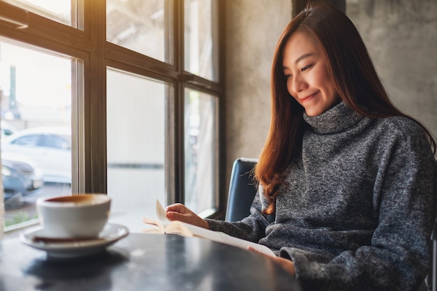 Closeup image of a beautiful woman holding and reading a book with coffee cup on the table