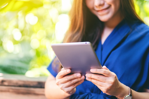 Immagine del primo piano di una bella donna che tiene e usa un tablet pc mentre è seduta in giardino