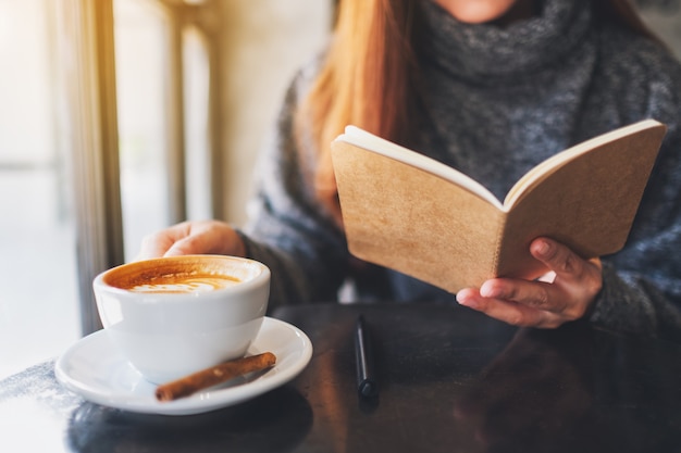 Closeup image of a beautiful woman reading a book while drinking coffee in the morning