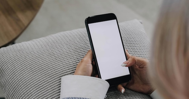 Closeup image Beautiful young Asian female using her smartphone while relaxing in her minimal living room a woman holding a mobile phone white screen mockup