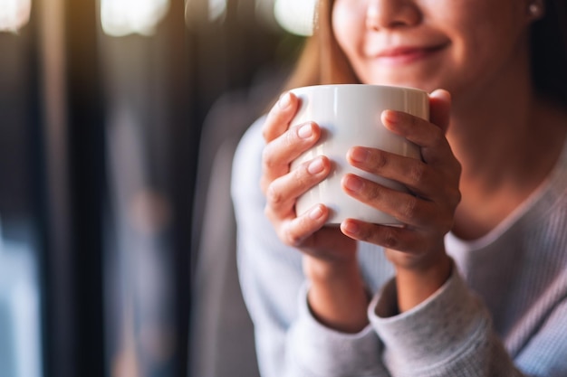 カフェでホットコーヒーを保持し、飲む美しい若いアジアの女性のクローズアップ画像