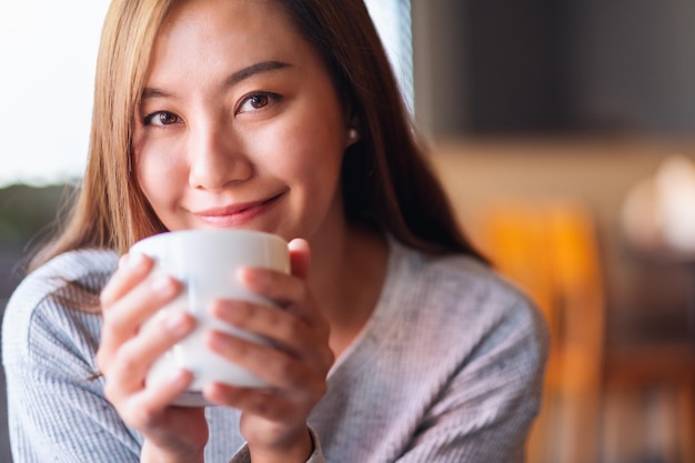 카페에서 뜨거운 커피를 들고 마시는 아름다운 젊은 아시아 여성의 클로즈업 이미지