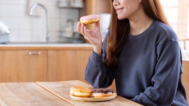 Immagine del primo piano di una bella giovane donna asiatica che tiene e mangia la ciambella a casa