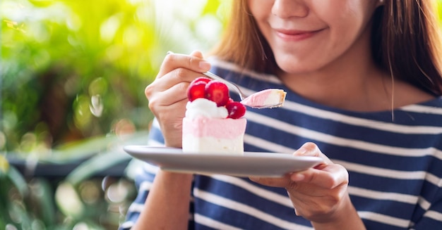 Closeup image of a beautiful young asian woman holding and eating a piece of strawberry cheese cake