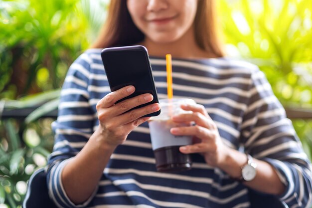 Immagine del primo piano di una bella giovane donna asiatica che tiene e utilizza lo smartphone mentre beve il caffè