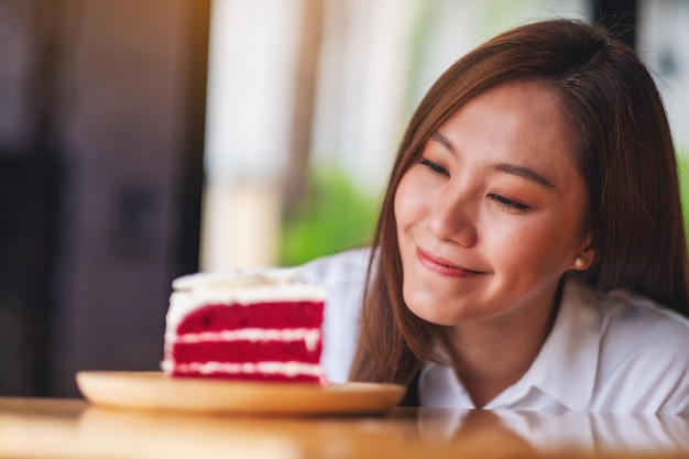 Closeup image of a beautiful young asian woman looking at a piece of red velvet cake in wooden tray on the table