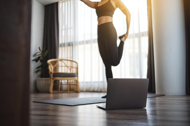 Closeup image of a beautiful young asian woman stretching leg while watching online workout tutorials on laptop at home