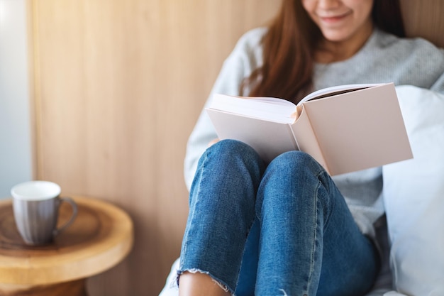 Closeup image of a beautiful young woman reading book in a white cozy bed at home