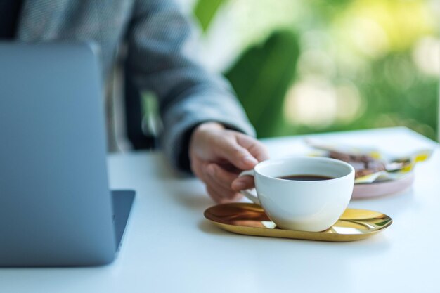 Closeup image of a business woman using and working on laptop computer while drinking coffee in office