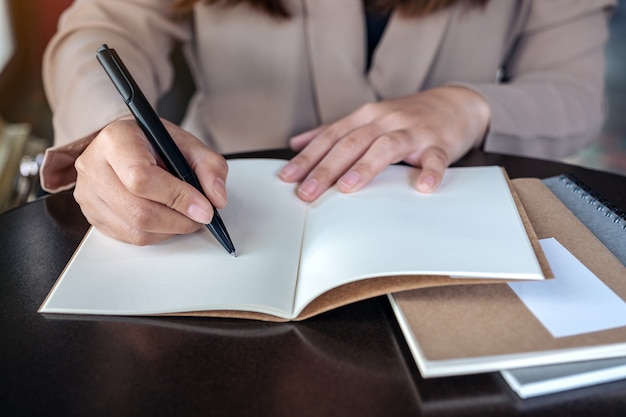 Closeup image of a business woman writing on blank notebook on wooden table