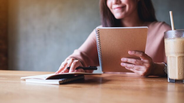 Photo closeup image of a businesswoman working and writing on a notebook on wooden table