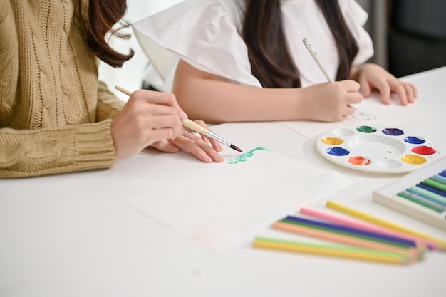 Closeup image of a caring Asian mom teaching her little daughter to paint