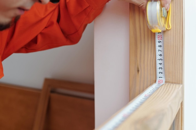 Photo closeup image of carpenter measuring wooden frame with rape measure before installing new windows in...