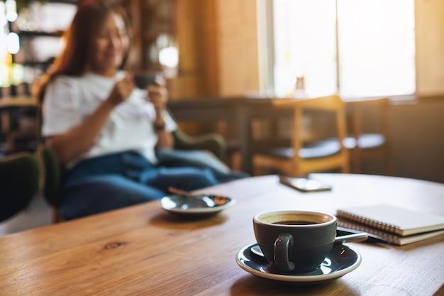 バックグラウンドで座っている女性とコーヒーカップと木製テーブルの本のクローズアップ画像