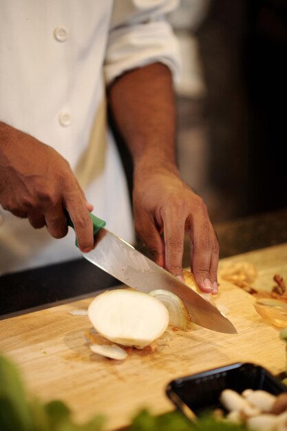 Closeup image of cook cutting fresh onion in thin slices