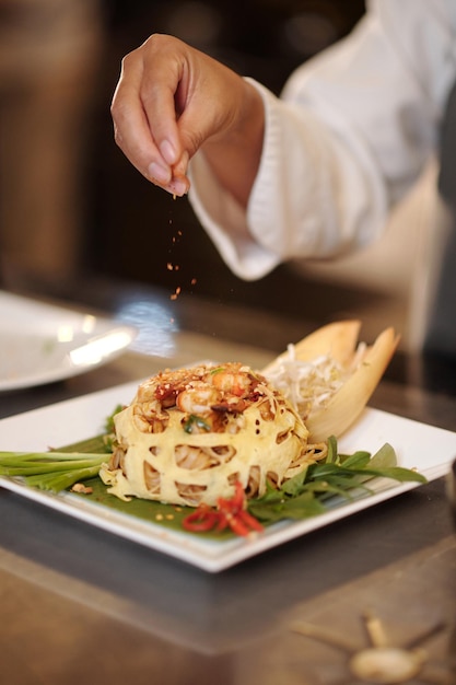 Closeup image of cook decorating garnished dish with pinch of smoked paprika