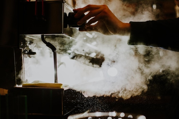 Photo closeup image of female barista using coffeemaking machine to steam milk in cafe