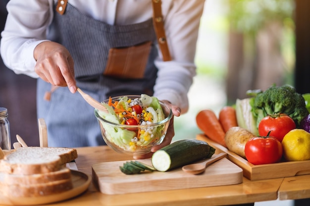 Photo closeup image of a female chef cooking fresh mixed vegetables salad in kitchen