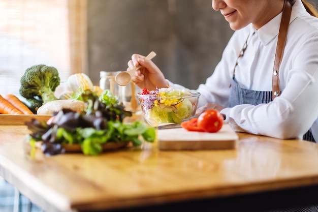 キッチンで食べるために新鮮な混合野菜サラダのボウルを調理し、保持している女性シェフのクローズアップ画像