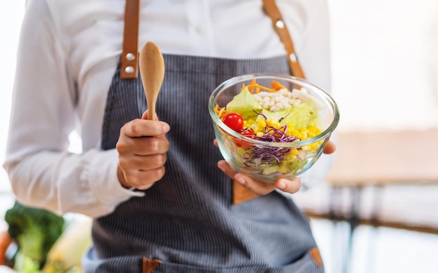 Closeup image of a female chef cooking and holding a bowl of fresh mixed vegetables salad to eat in kitchen