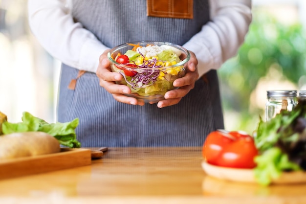 Closeup image of a female chef cooking and holding a bowl of fresh mixed vegetables salad in kitchen