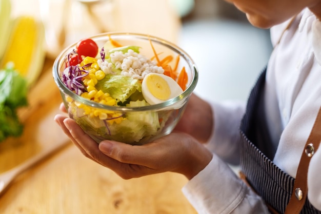 Closeup image of a female chef cooking and holding a bowl of fresh mixed vegetables salad in kitchen