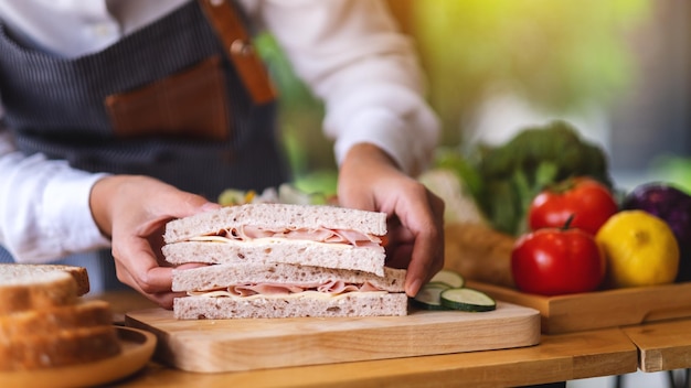 Closeup image of a female chef cooking and holding a piece of whole wheat ham cheese sandwich in kitchen