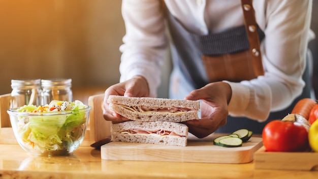 Closeup image of a female chef cooking and holding a piece of\
whole wheat ham cheese sandwich in kitchen