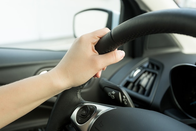 Closeup image of female hand holding car steering wheel