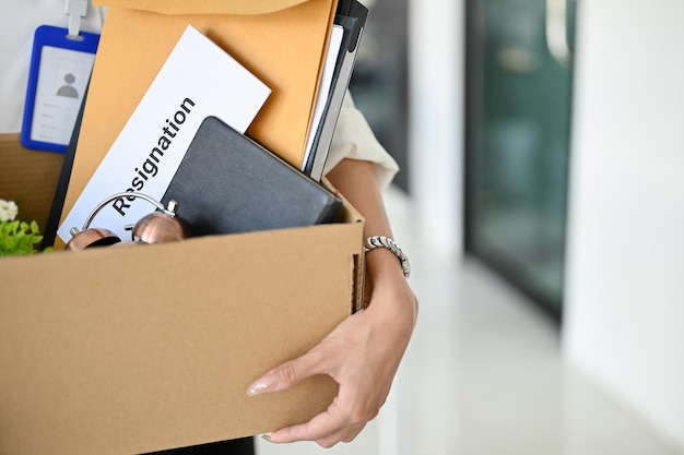 Closeup image of a female office worker holding a box with her belongings and a resignation letter