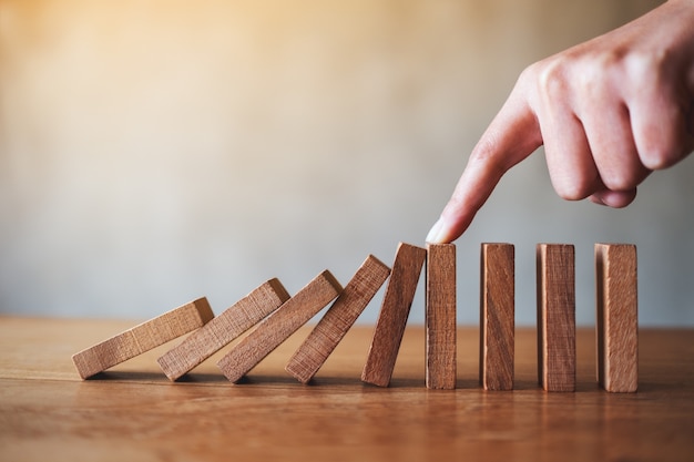 Closeup image of a finger try to stopping falling wooden dominoes blocks for business solution concept