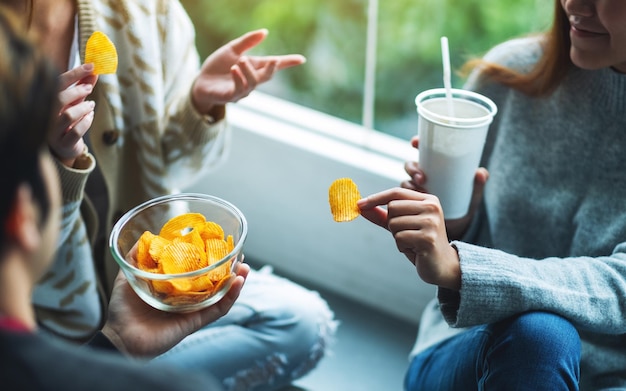 Closeup image of friends talking drinking and eating potato chips together