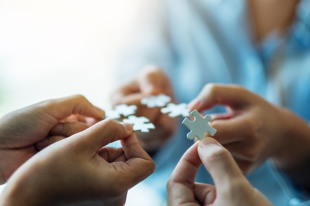 Closeup image of a group of people holding and putting a piece of white jigsaw puzzle together