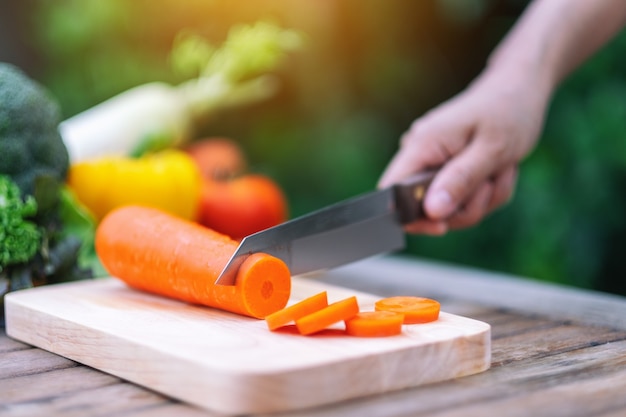 Closeup image of a hand cutting and chopping carrot by knife on wooden board