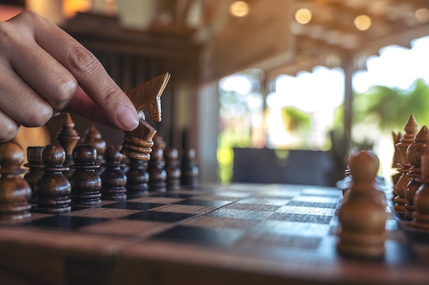 Closeup image of a hand holding and moving a horse in wooden chessboard game