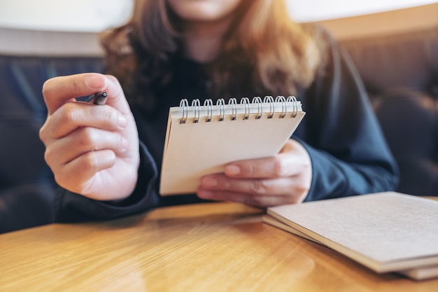 Closeup image of a hand holding and writing on blank notebook on table in cafe