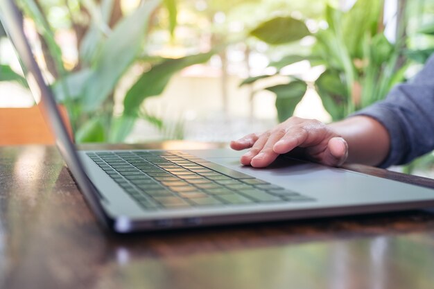 Closeup image of hand using and touching on laptop touchpad on wooden table