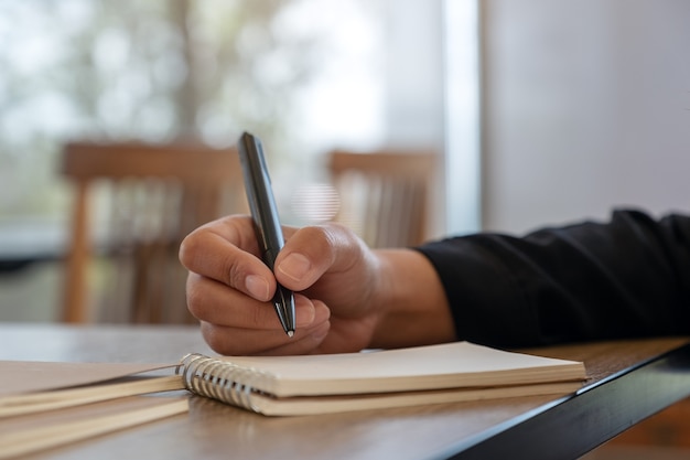 Closeup image of a hand writing on blank notebook on wooden table